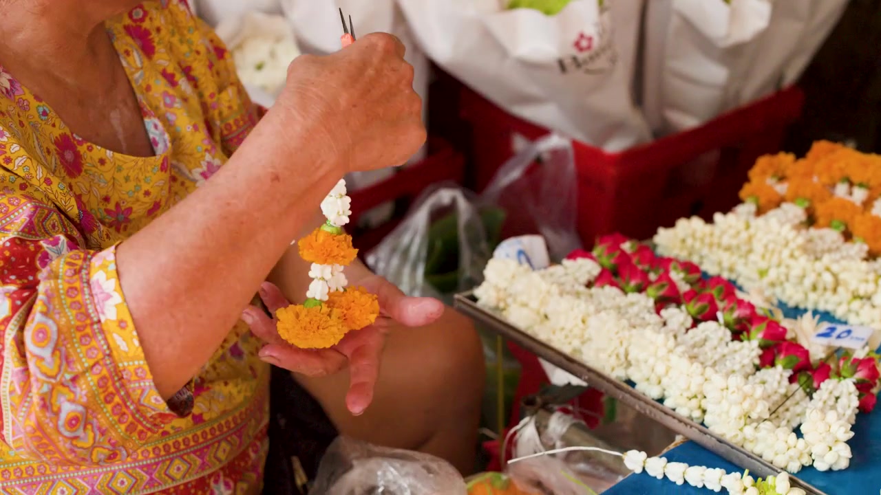 Primo piano di mani che infilano ghirlande di gelsomino e calendula a Pak Khlong Talat, Bangkok