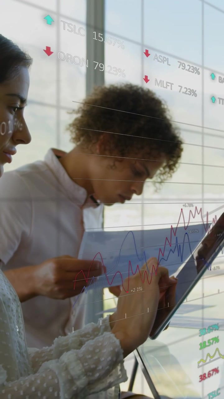 Vertical video: Woman tapping tablet while man comparing pages, finance charts emerging for review