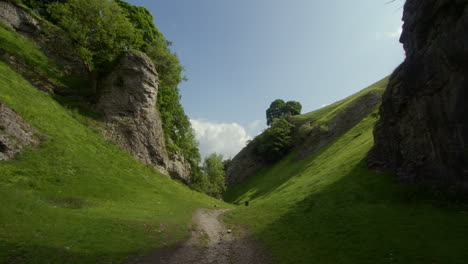 view of the path at cave dale going past the steep limestone cliff , castleton