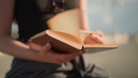 close-up of individual holding a book as pages flip rapidly to the right due to wind, the individual removes her hand, allowing pages to flip again as the background remains blurred