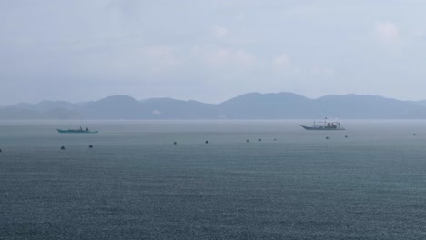 Local-fishing-and-transport-boats-heading-for-shelter-during-rainy-downpour-and-grey-cloudy-skies-in-Coron-Bay-of-Palawan,-Philippines