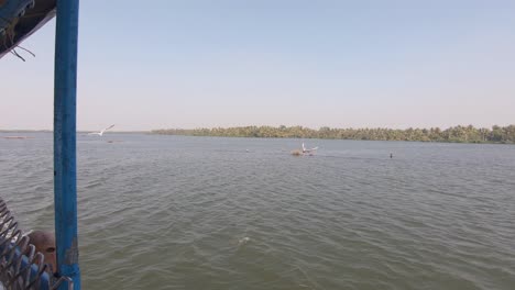 Boat-sailing-across-river-islets-followed-by-seagulls,-Alappuzha