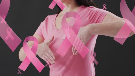 Animation-of-pink-ribbons-over-caucasian-woman-with-pink-ribbon-on-black-background