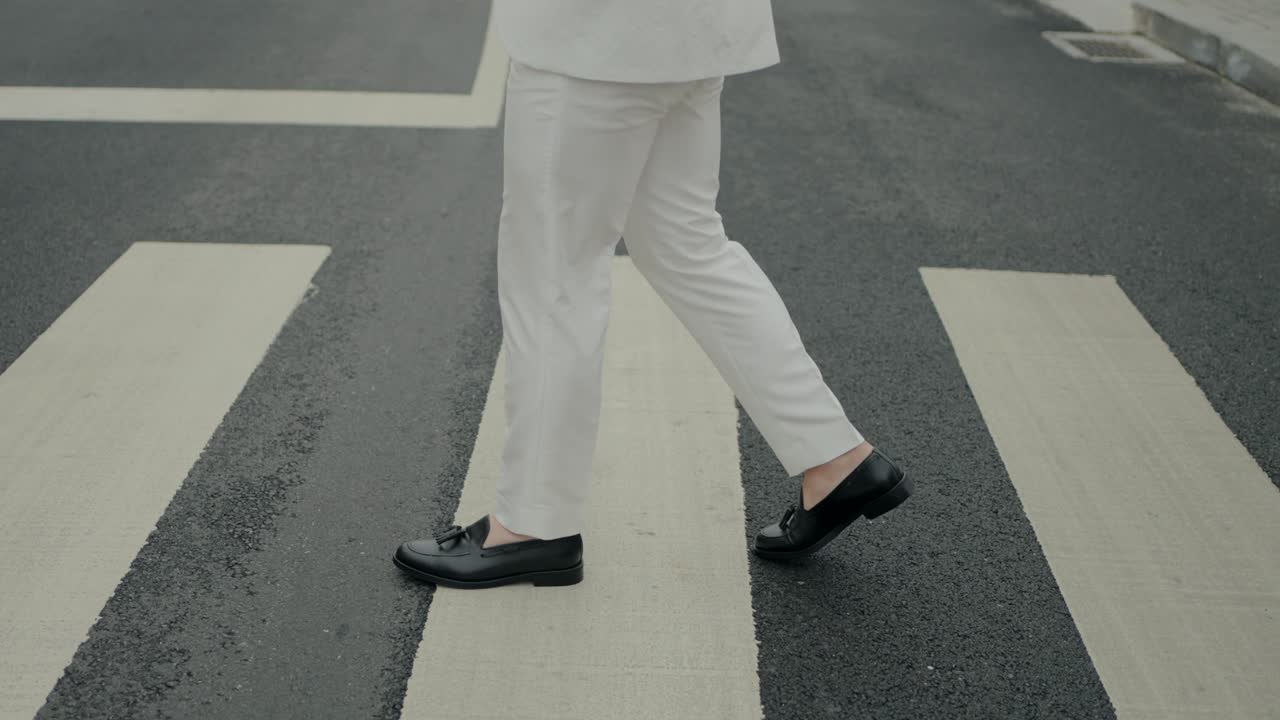novio en pantalones blancos y zapatos negros cruzando una calle, destacando el estilo moderno de la boda