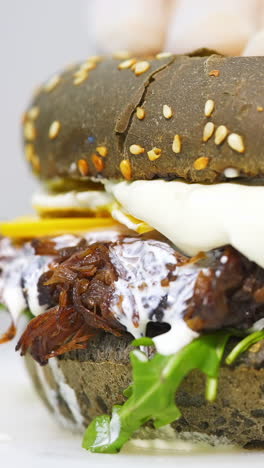 close-up of a delicious black bun burger with pulled pork and creamy sauce