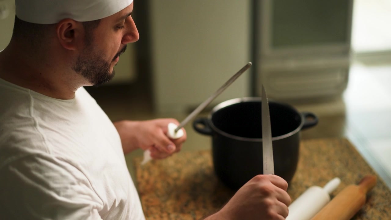 Uno chef esperto usa un acciaino per affilare la lama di un coltello da cucina.