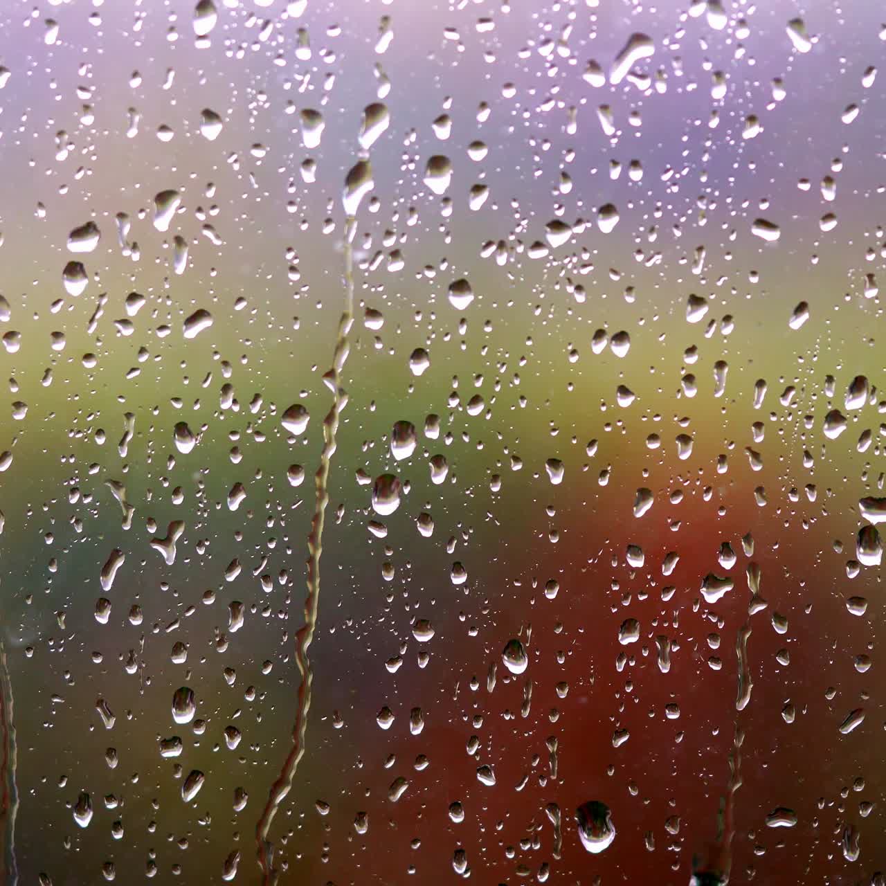 Water droplets on glass surface. Rainy weather. Raindrops on window. Water drops flowing down the window on blur colorful background. Close-up.