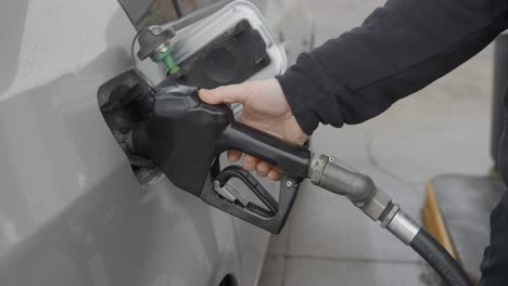 estación de servicio hombre caucásico blanco con anillo de bodas llenando un auto plateado insertando una boquilla de gas en el tanque y luego ajustando el mecanismo automático de la bomba de una sola vez y retrocediendo