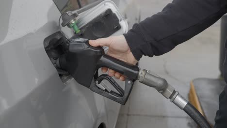 gas station white caucasian man with wedding ring filling up silver car inserting gas nozzle in tank then setting pump auto mechanism in one shot then standing back