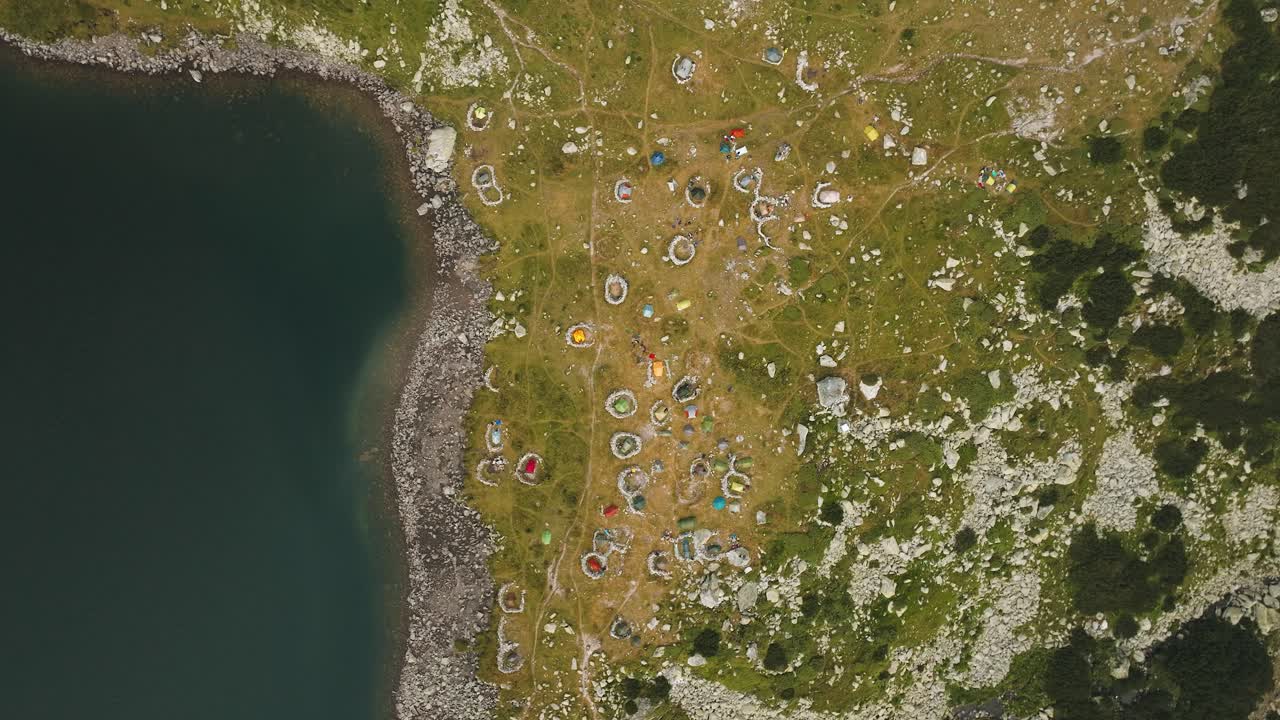 Hiker tents of different colors, spread near a glacial lake, top aerial view