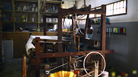 a young man operating a floor treadle loom inside