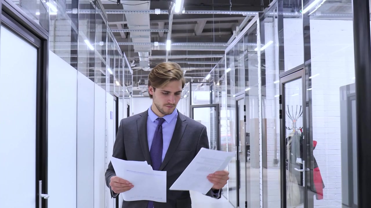 Young Businessman Walking and Reviewing Documents in Modern Office