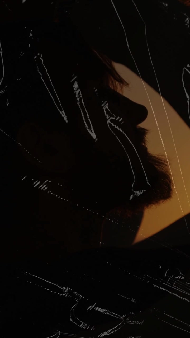Video verticale: Uomo barbuto che annuisce con il mento al tramonto sul mare, il sole che colpisce il bordo, con un effetto pellicola che modella l'inquadratura.