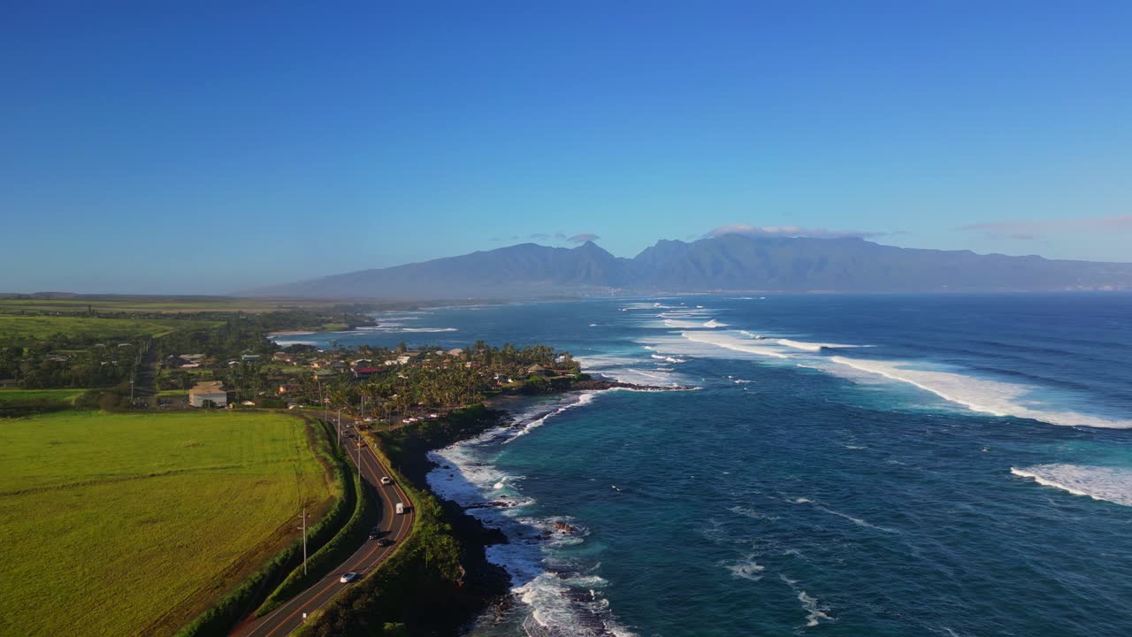 Una squisita ripresa aerea cattura la bellezza mozzafiato di Maui, nelle Hawaii, mostrando una strada costiera tortuosa, rigogliosi campi verdi e il vivace oceano turchese con onde che si infrangono.