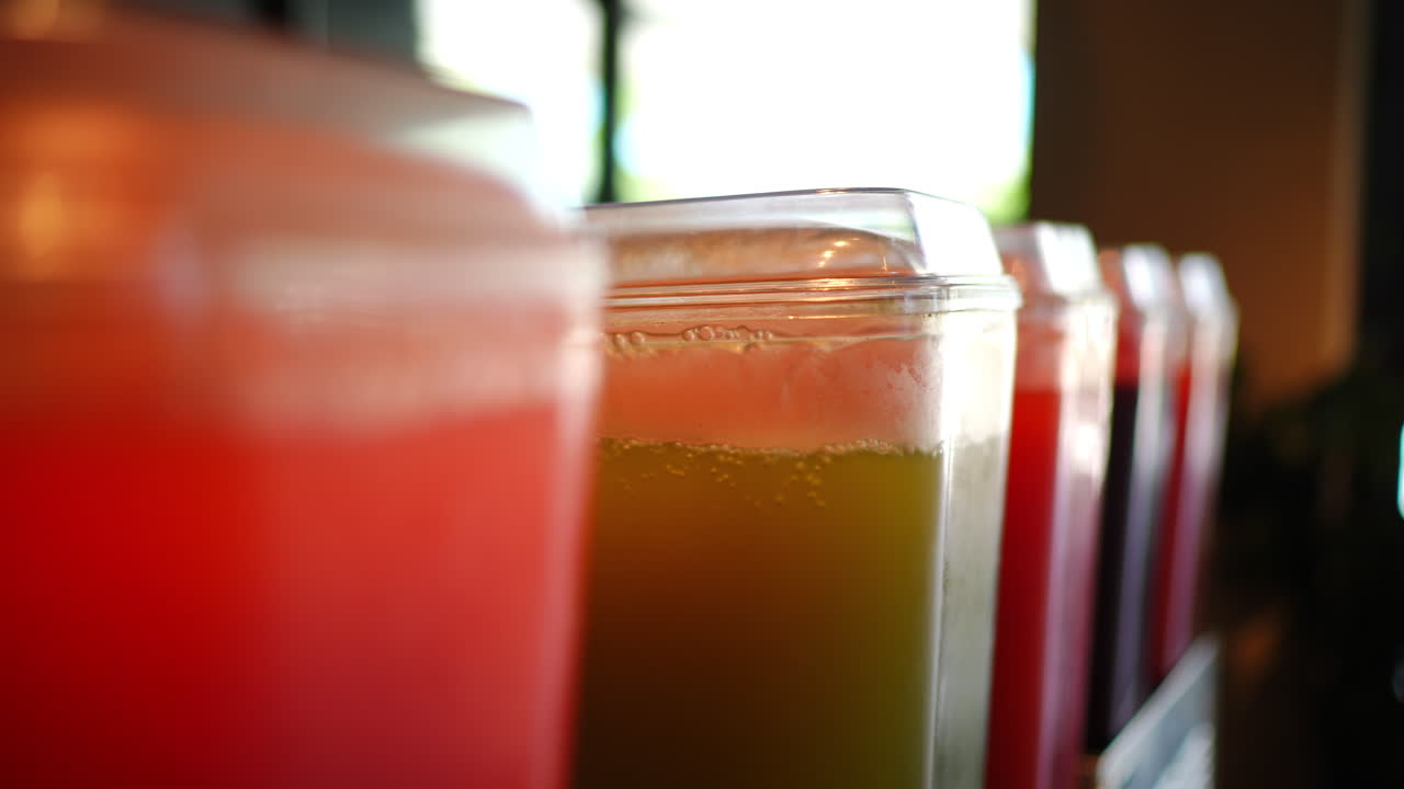 Colorful juice dispensers display fresh beverages with a focus on vibrant red and green drinks, highlighting refreshing choices in a cafe or juice bar