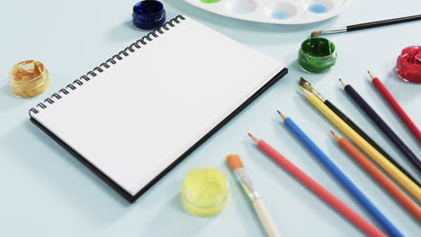 primer plano del cuaderno, pinceles y pinturas sobre fondo azul, en cámara lenta