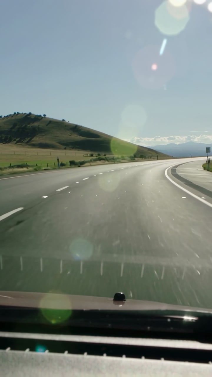 Vertical video: Driving car taking right curve on rural road, sun flaring, hood and dash visible