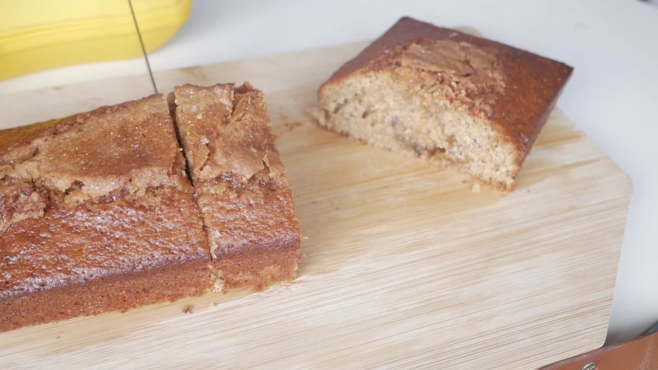 Person slicing fresh homemade banana bread loaf on a wooden board, showing texture and golden crust