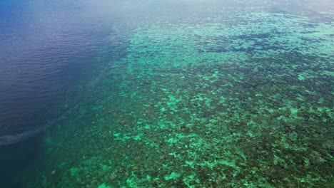 Drone-flying-over-a-shallow-coral-reef-with-a-drop-off-into-deep-blue-water