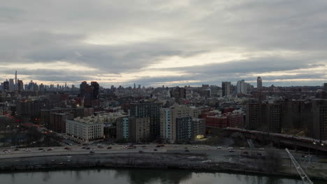 Aerial-view-over-the-river,-towards-traffic-and-a-train,-in-gloomy-Harlem,-New-York