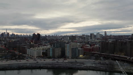 Vista-Aérea-Sobre-El-Río,-Hacia-El-Tráfico-Y-Un-Tren,-En-Gloomy-Harlem,-Nueva-York