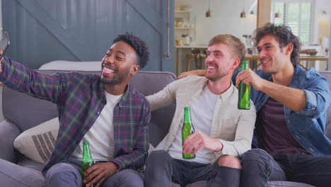 multi-cultural group of male friends sitting on sofa at home drinking beer and posing for selfie