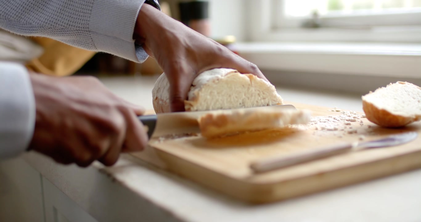 African American man in plaid shirt slicing loaf on counter with serrated knife preparing breakfast