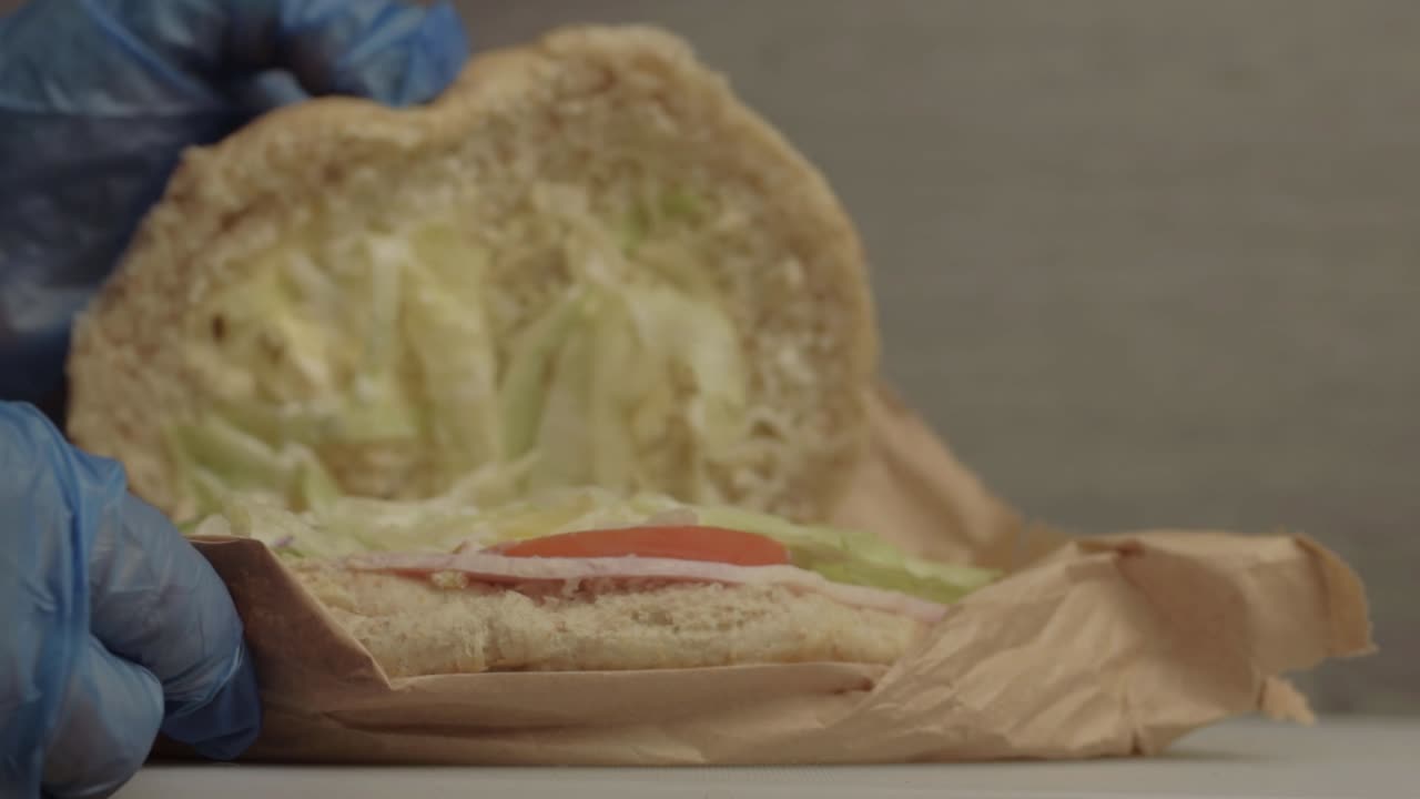 Hands preparing salad sandwich with hygiene gloves close up
