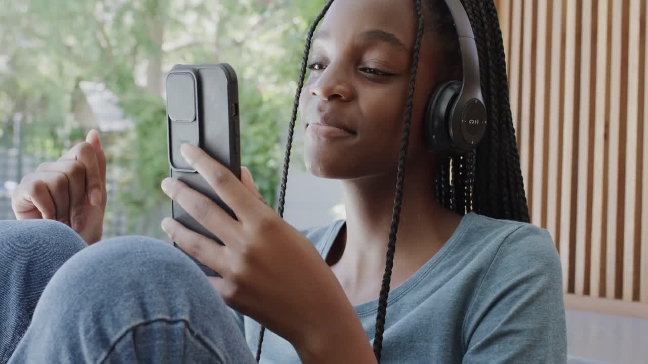 Ragazza adolescente afroamericana felice con le cuffie che ascolta musica con lo smartphone.