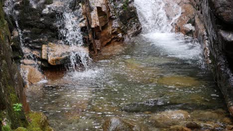 Camera-tils-revealing-a-rocky-stream-being-fed-by-a-waterfall,-running-down-the-stone-walls-of-the-Flume-Gorge-in-New-Hampshire