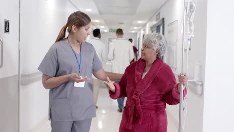 serious diverse female nurse talking to senior patient with drip walking in slow motion, unaltered