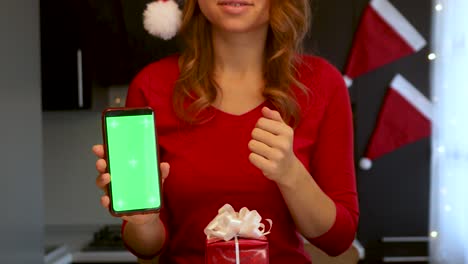 a girl in a new year's red suit in the kitchen shows a smartphone with a green screen