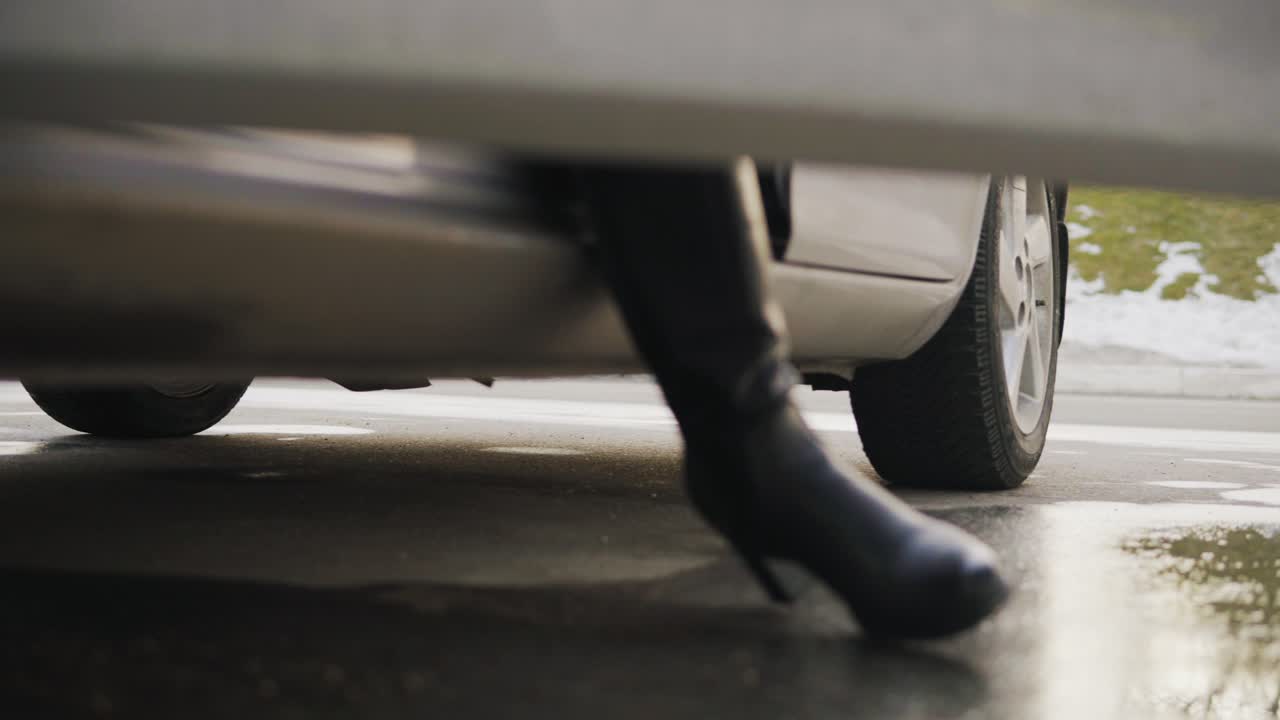 Closeup view of woman's legs in high heels getting out of car. Wet ground after rain