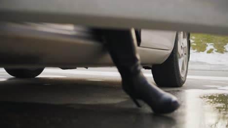 Nahaufnahme-Der-Beine-Einer-Frau-In-High-Heels,-Die-Aus-Dem-Auto-Steigt.-Nasser-Boden-Nach-Regen