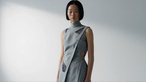 a captivating fashion showcase featuring a model in a sophisticated gray dress with unique cutouts, emphasizing modern design and style in a minimalistic setting