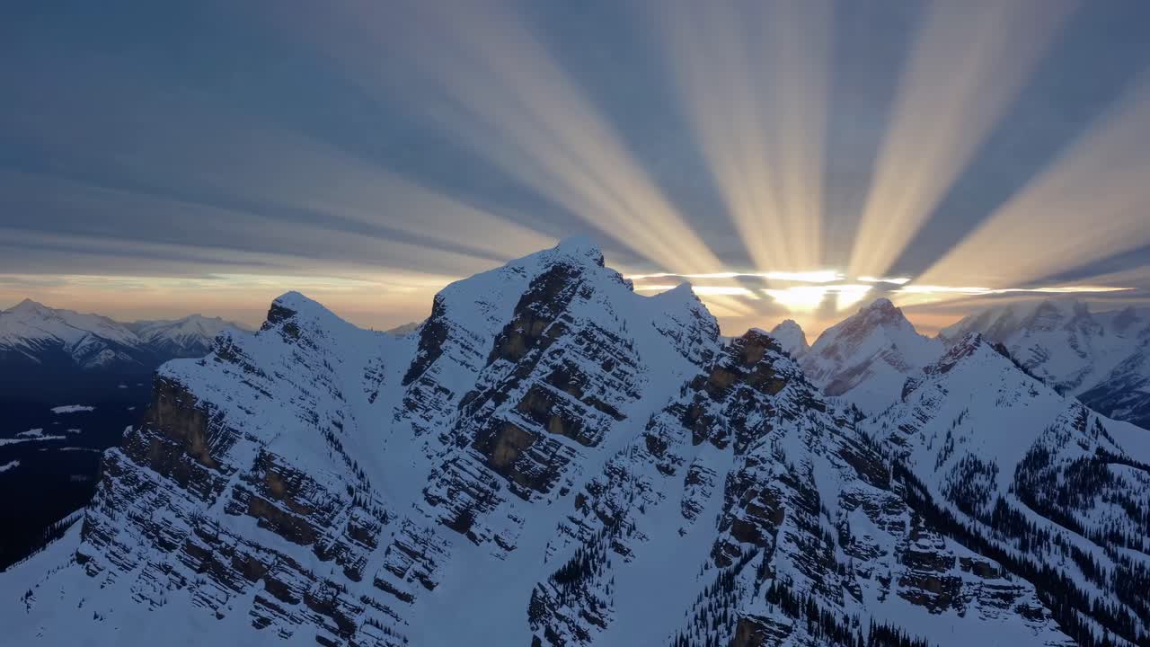 Aerial video captures dramatic sunrise rays over snow-capped mountains, highlighting rugged peaks