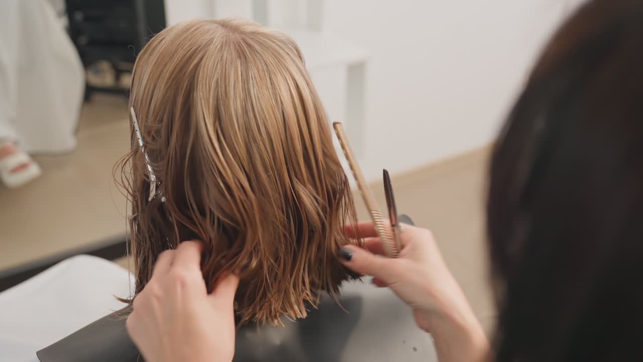 Estilista atento recortando un corte bob trenzado y húmedo, con las manos separando las trenzas texturizadas con un peine y unas tijeras sobre una capa negra en un salón moderno y luminoso; primer plano del corte de precisión y los detalles finales.