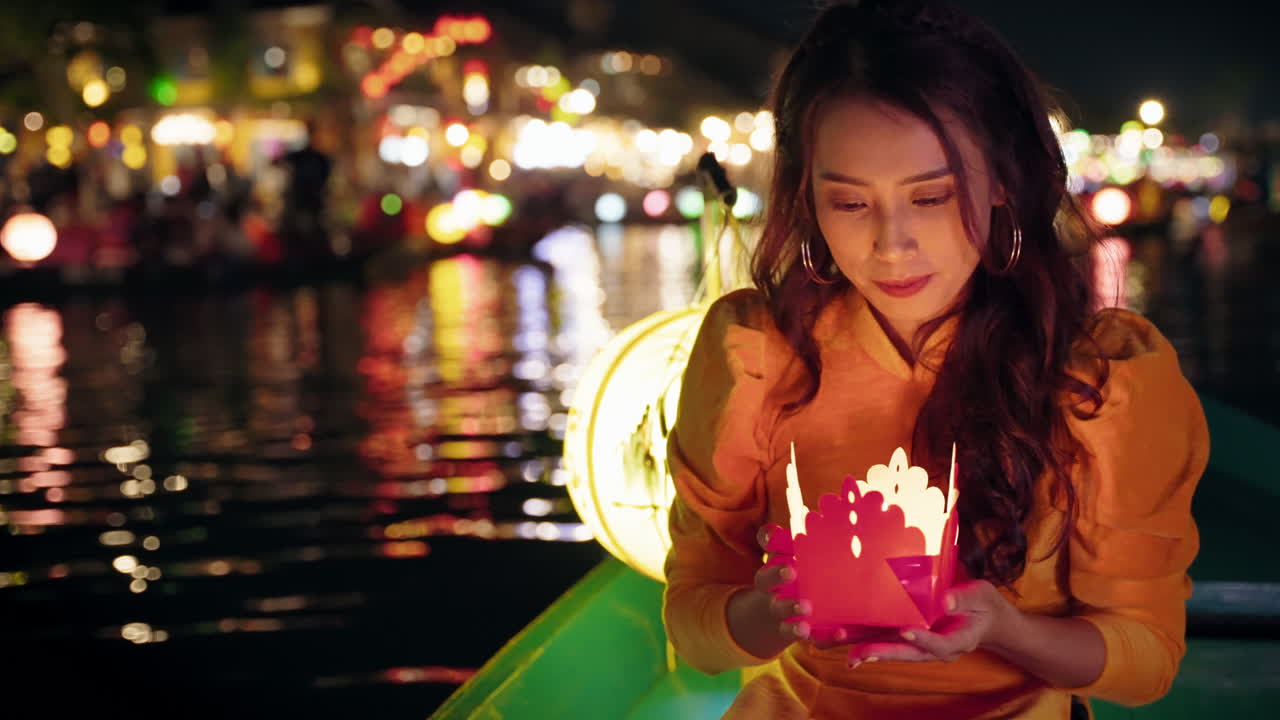 Menina asiática feliz segurando uma vela em um barco no mercado noturno de Hoi An