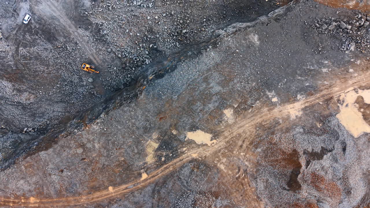 Daytime construction at site. Heavy machinery is operating on a construction site. The ground is uneven with various materials spread across the area
