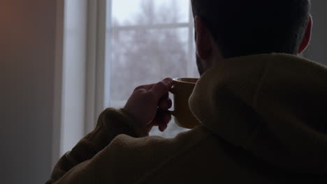 Man-drinking-delicious-coffee-while-watching-through-home-window,-back-view