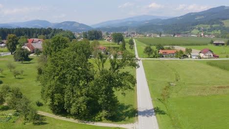 aerial view of slovenj gradec town in slovenia with tractor, homes, farms, and roads below, drone dolly in reveal shot, license plates and tractor operator blurred