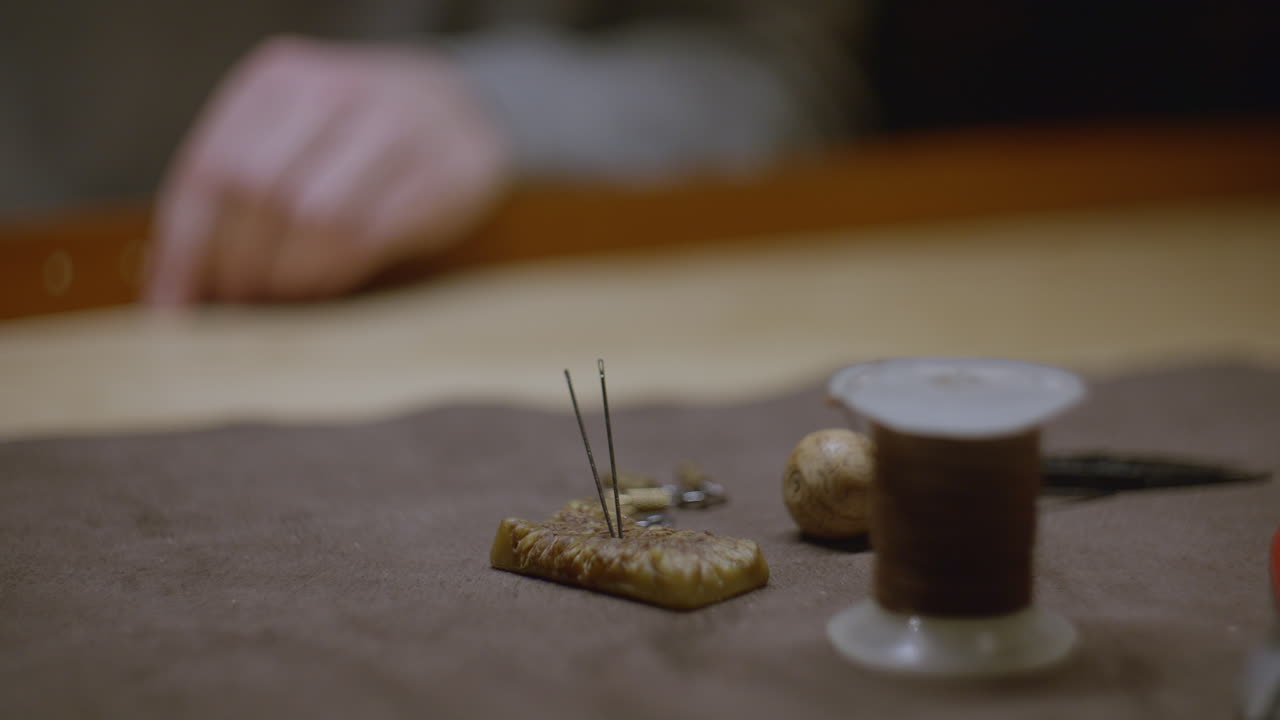 A set of sewing needles stuck into a beeswax block, surrounded by leathercraft tools such as thread, an awl, and metal fasteners.