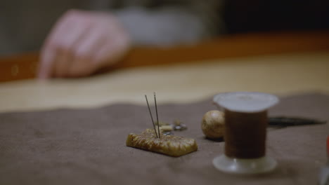 a set of sewing needles stuck into a beeswax block, surrounded by leathercraft tools such as thread, an awl, and metal fasteners.