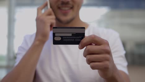 Young-man-holding-credit-card-and-talking-on-phone.