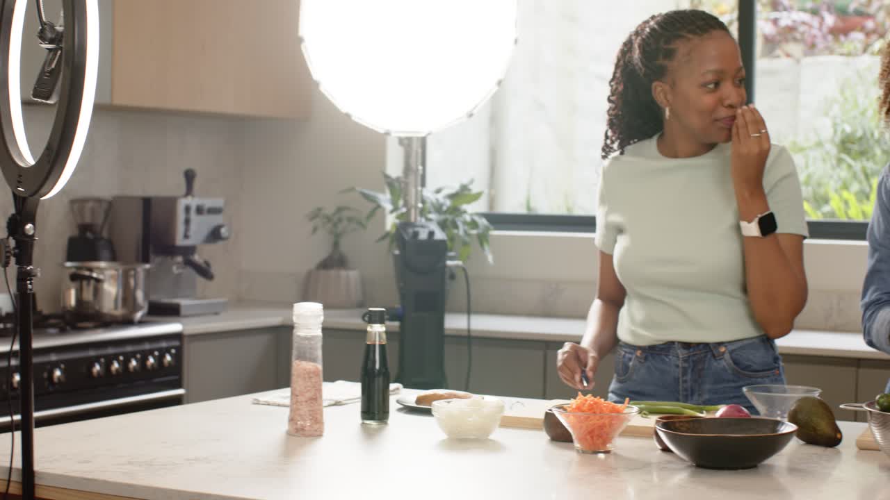 Donne afroamericane che tagliano su un'isola da cucina sotto una ring light, condiscono e assaggiano per una dimostrazione