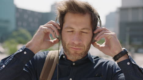 portrait of handsome young caucasian man in sunny urban city street listening to music wearing headphones enjoying relaxed urban city travel lifestyle