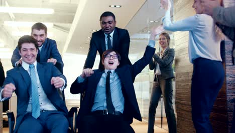 cuatro empresarios multiétnicos divertidos montan sillas en el pasillo del edificio corporativo. los colegas aplauden y aplauden. celebran el cierre del acuerdo.