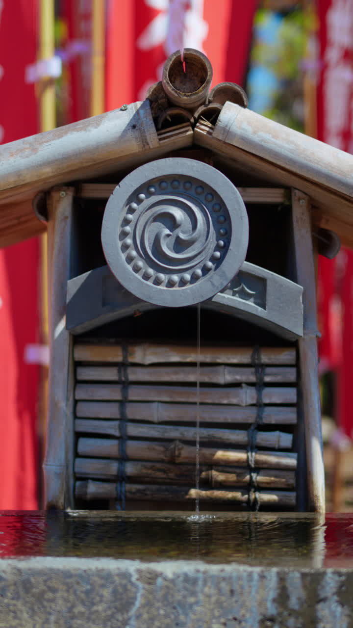 Close up of a small water fountain surrounded by red flags at the Senso-ji temple in Asakusa, Tokyo, Japan. Vertical. Translation: "Dedication"
