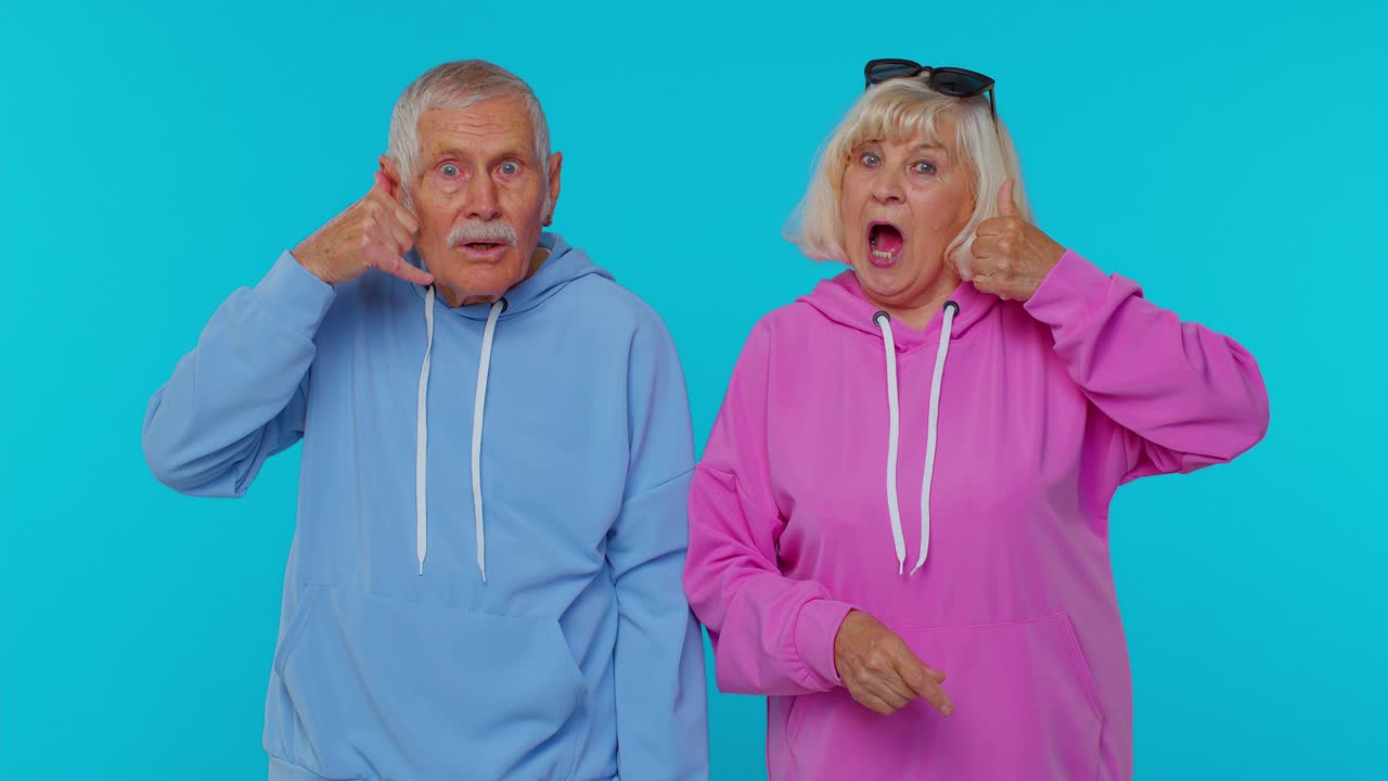 Senior grandfather grandmother looking at camera doing phone gesture like says hey you call us back