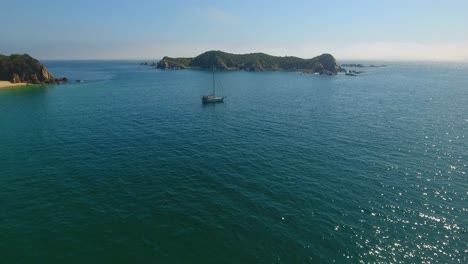 Vorwärts-Fliegend,-Um-Herauf-Ansicht-Des-Weißen-Segelbootes-Im-Ruhigen-Ankerplatz-Mit-Nahe-Gelegener-Insel-Im-Schimmernden-Wasser-Zu-Schließen